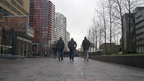 Fußgänger,-Die-Auf-Einem-Gepflasterten-Fußweg-Mit-Farbigen-Gebäuden-Im-Vordergrund-An-Der-Kamera-Vorbeigehen