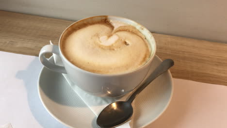 Weiße-Kaffeetasse-Mit-Gehörter-Latte-Art-Auf-Milchschaum,-Stehend-Auf-Einem-Holzbrett