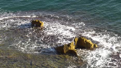 Blue-Ocean-waves-break-over-reef-with-large-rocks,-slow-motion