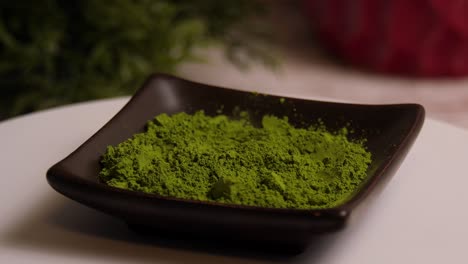 Grünes-Matcha-Teepulver-In-Einer-Schüssel,-Die-Auf-Einem-Weißen-Teller-Rotiert