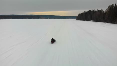 Toma-Aérea-De-Seguimiento-De-Un-Hombre-Conduciendo-Su-Moto-De-Nieve-En-Indalsalven-En-Timra,-Sundsvall,-Suecia