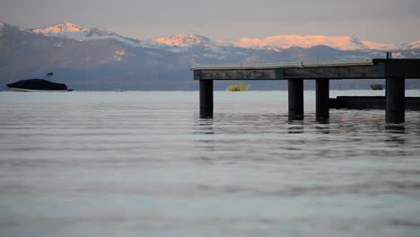 Ruhige-Wellen-Krachen-Gegen-Den-Pier-In-Lake-Tahoe-Mit-Schneebedeckten-Bergen-Im-Hintergrund