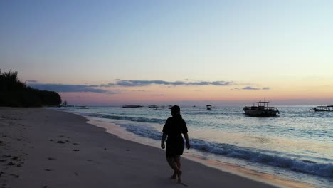 Lonely-tourist-girl-walking-around-exotic-beach-of-Seychelles-at-twilight,-watching-beautiful-sky-with-blue-yellow-colors-and-silhouettes-of-boats-floating