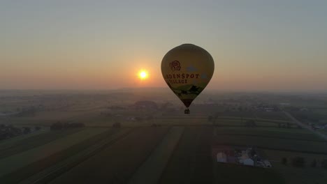 Sonnenaufgang-Eines-Heißluftballons-An-Einem-Nebligen-Morgen-über-Amischem-Ackerland,-Wie-Von-Einer-Drohne-Gesehen