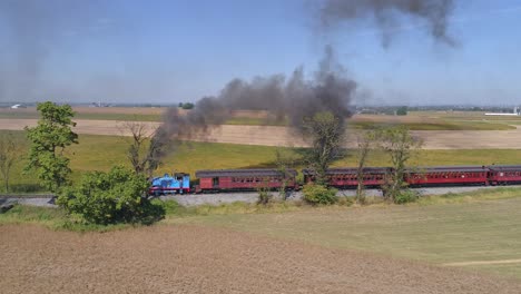Aerial-View-of-Thomas-the-Train-Puffing-Black-Smoke-and-Pulling-Passenger-Cars-full-of-Happy-Children-on-a-Sunny-Day-as-Seen-by-a-Drone