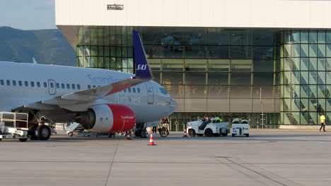 Un-Avión-Boeing-737-Perteneciente-A-Las-Líneas-Aéreas-Escandinavas-Estacionado-En-La-Terminal-Dividida-Con-Los-Pasajeros-Y-El-Personal-De-Apoyo-En-Tierra-En-El-Fondo