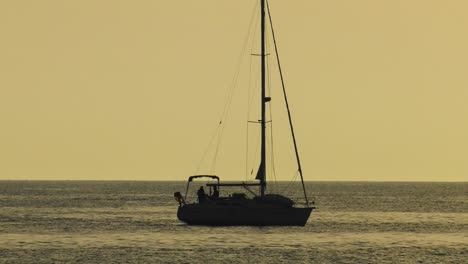 Sailboat-at-dawn,-yacht-silhouetted-on-silver-sea,-slow-motion
