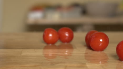 Tomates-Cherry-Rojos-Caen-Sobre-Una-Tabla-De-Cortar-Con-Salpicaduras-De-Agua,-Apple-Prores-Camión-Con-Cámara-En-Cámara-Lenta-De-Izquierda-A-Derecha