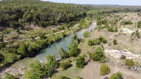 Fast-pan-right-to-reveal-swimming-area,-flying-towards-and-then-up-the-travel-of-the-river---Aerial-footage-of-the-Blanco-river-in-Wimberly,-TX
