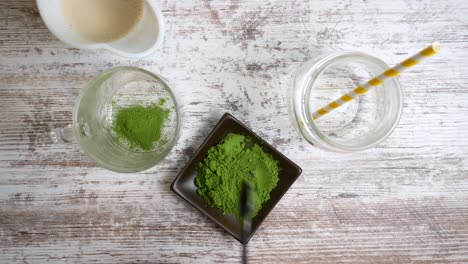Spooning-green-tea-matcha-powder-into-a-glass-cup-then-pouring-hot-water-into-the-glass