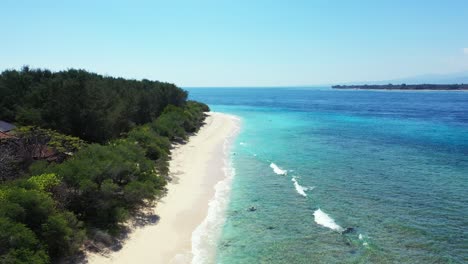 Tranquila-Playa-Blanca-De-Isla-Tropical-Con-Exuberante-Vegetación-Al-Amanecer,-Bañada-Por-Olas-Blancas-De-Mar-Azul-Azulado-En-Un-Cielo-Azul-Brillante-En-Bali