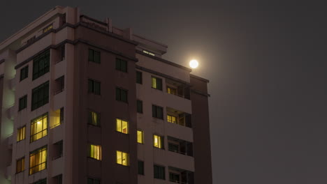 Time-Lapse-of-Full-Moon-rising-over-a-residential-building-as-lights-are-switched-off-and-on-at-night