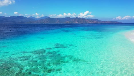 Colorful-sea-texture-with-blue-turquoise-sea-water-over-beautiful-pattern-of-coral-reefs-and-rocks-surrounded-by-high-mountains-of-islands-of-Indonesia
