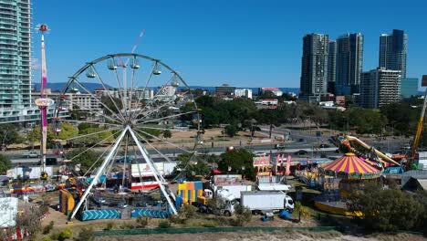 Aerial-view-of-a-beach-side-carnival-next-to-a-busy-main-road-with-buildings-in-the-background