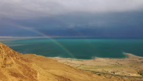Fly-to-Rainbow-in-front-of-the-Dead-Sea-view,-desert-cliff-foreground,-aerial-shot