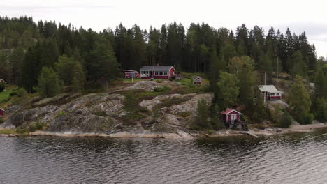 Red-traditional-cabins-on-an-island-in-Sweden,-aerial-zoom-in