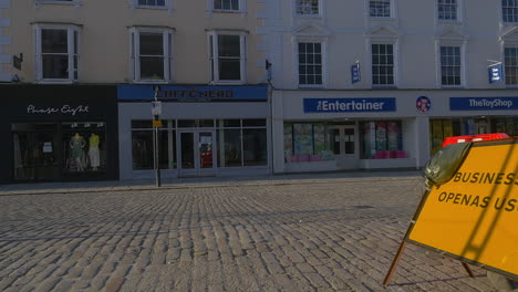 Business-open-as-usual-sign-in-empty-UK-cobblestone-street,-slow-pan