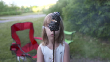Little-girl-holding-up-a-burnt-marshmallow-on-a-stick