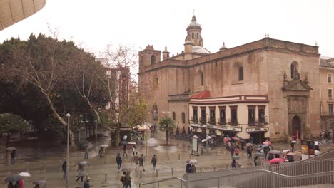 SLOWMO,-People-walk-past-church-in-rainy-Seville,-seen-from-vantage-point