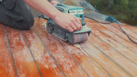 Belt-sanding-roof-planking-repair-rubbing-hand-over-planks