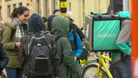 Deliveroo-rider-waits-among-schoolchildren-in-the-busy-city-centre-for-next-order,-Ghent,-Belgium