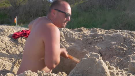 A-man-getting-out-of-the-hole-he-dug-on-the-beach,-treasure-hunting---mid-shot