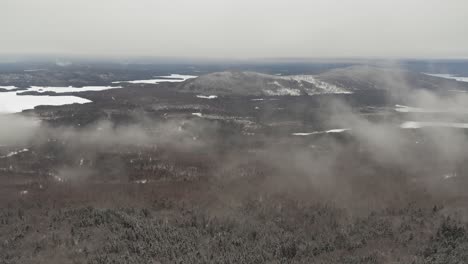 Low-hanging-clouds-over-an-endless-winter-forest-with-lakes-and-hills-AERIAL