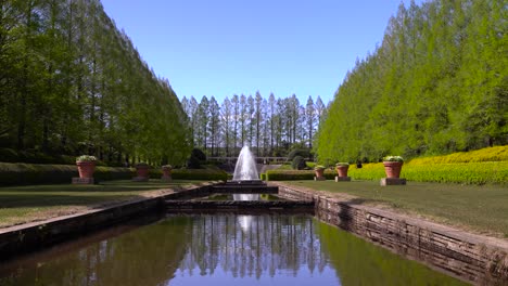 Die-Wunderschöne-Landschaft-Eines-öffentlichen-Parks-Mit-Vielen-Grünen-Bäumen-Und-Einem-Springbrunnen-In-Der-Mitte-An-Einem-Sonnigen-Blauen-Himmel-–-Weitwinkelaufnahme
