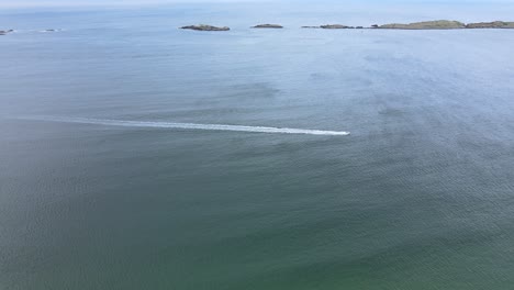 Ein-Schnellboot,-Das-Sich-Schnell-über-Das-Große-Blaue-Meer-In-Irland-Bewegt,-Mit-Einer-Vulkaninsel-Im-Hintergrund-–-Luftaufnahme