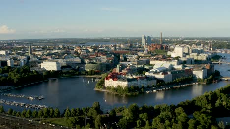Slow-aerial-pan-of-the-Helsinki-waterfront-reflecting-on-the-water-below-at-sunset,-Finland