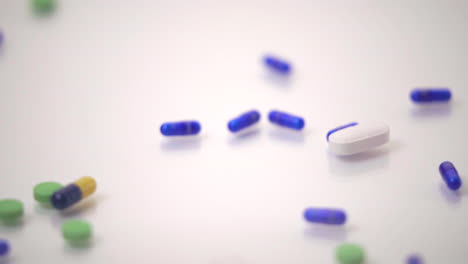 Slow-Motion-Macro-of-Pill-Varieties-Sliding-onto-One-Blue-and-Yellow-Pill-on-White-Background