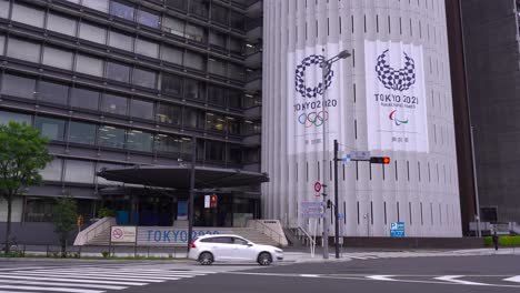 Schild-Mit-Den-Olympischen-Spielen-2020-In-Tokio-An-Der-Fassade-Eines-Gebäudes-Mit-Autoverkehr-–-Blick-Auf-Die-Straße