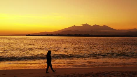 Silhouette-Eines-Mädchens,-Das-Nach-Sonnenuntergang-Allein-Am-Sandstrand-Spaziert,-Mit-Einem-Wunderschönen,-Farbenfrohen-Gelben-Himmel,-Der-Sich-über-Das-Lebendige-Wasser-Des-Meeres-In-Myanmar-Spiegelt