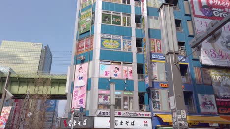 Slow-motion-pan-over-multi-story-maid-cafe-and-anime-stores-on-sunny-day-in-Tokyo,-Japan