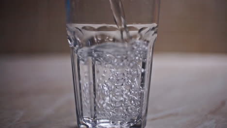 Nahaufnahme-In-Zeitlupe,-Die-Ein-Transparentes-Glas-Mit-Kaltem-Wasser-Aus-Einer-Glasflasche-Füllt,-Auf-Einer-Laminatoberfläche-In-Einer-Küche