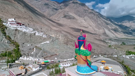 aerial-view-of-a-tall-lord-budha-statue-with-an-old-monastery-in-background-situated-over-a-mountain-at-a-distance