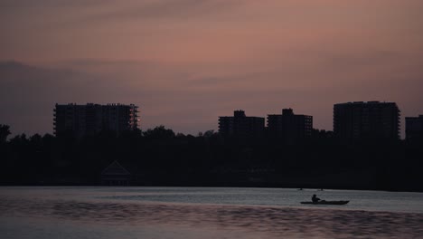 Silhouette-Von-Menschen-Auf-Einem-Boot-Am-Lake-Of-Nations-Mit-Gebäuden-Im-Hintergrund-In-Sherbrooke,-Quebec,-Kanada-Bei-Sonnenuntergang---Weitwinkelaufnahme