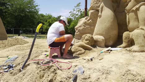 Man-Working-On-A-Sand-Figure-Of-A-Baby-For-Sand-Festival-In-Burgas,-Bulgaria---side-view,-zoom-in-shot