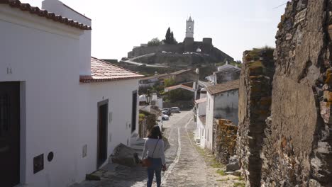 Mujer-Caminando-En-La-Calle-Del-Pueblo-De-Monsaraz-Con-Casas-Blancas-En-Alentejo,-Portugal