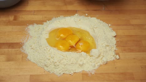 Pouring-eggs-into-a-mound-pile-of-flour-over-a-wooden-surface---High-angle-medium-shot