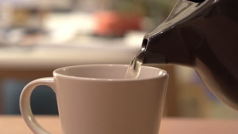 Close-up-shot,-pouring-hot-tea-from-a-black-teapot-into-a-white-cup