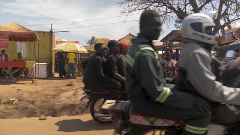 Two-African-women-stand-along-side-a-busy-road-while-a-motor-bike-taxi-drops-off-passengers-in-Uganda