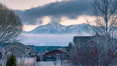 Two-layers-of-clouds-moving-in-opposite-directions-in-front-of-snowy-mountains-beyond-a-suburban-neighborhood---static-time-lapse