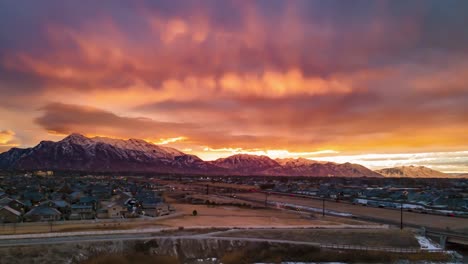 Sunrise-casts-orange-rays-of-sun-into-the-colorful-sky-and-cloudscape-above-the-waking-city-and-highway-traffic---aerial-hyperlapse