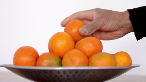 Hombre-Tratando-De-Elegir-Una-Fruta-Naranja-De-Un-Tazón-De-Naranjas-Y-Mandarinas-Que-Promueven-Una-Alimentación-Saludable-Almacen-De-Metraje-De-Video
