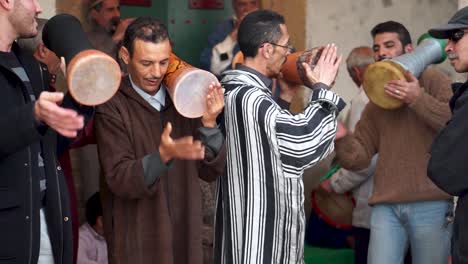 With-rhaita-or-mizmar-musicians-in-the-background,-closeup-of-men-playing-drums,-dance,-and-chant-as-they-fall-into-a-trance-at-a-Sufi-ceremony-in-Essaouira,-Morocco