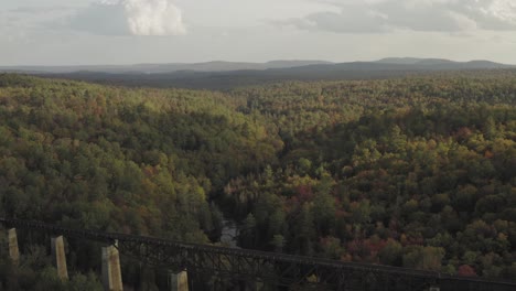 Railroad-Trestle-in-the-forest-crossing-a-winding-stream-with-early-fall-foliage-at-sunset-AERIAL-REVEAL