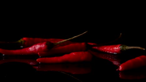 Falling-Red-Peppers-On-Wet-Surface-Against-Black-Background