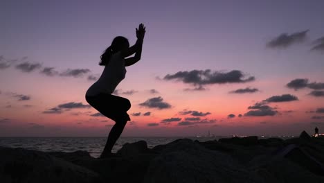 Silhouettenaufnahme-Einer-Frau,-Die-Yoga-Im-Stehen-Mit-Verschränkten-Beinen-Und-Armen-Praktiziert,-Aufgenommen-In-Der-Dämmerung-Am-Meer