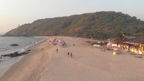 People-stroll-along-Arambol-beach,-serene-ocean-waters